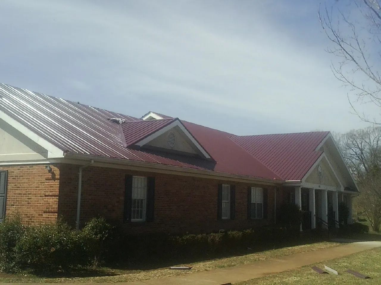Red metal roof with gabled entries on a long brick building, from a Hail Damage Roof Repair job in Oakland